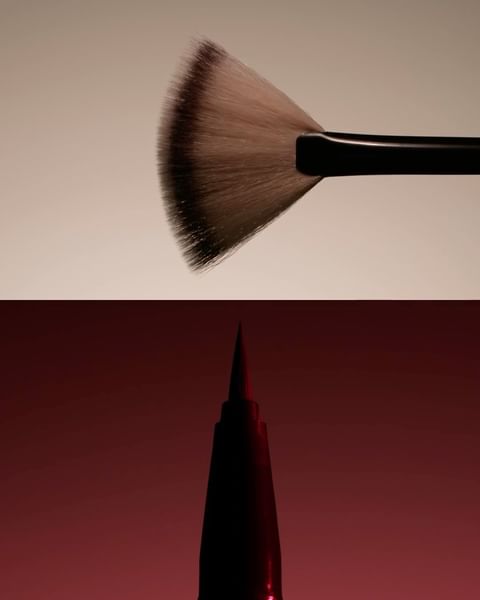 Close-up shot makeup brushes; a large fan brush with brown-tipped bristles and a black handle, and a black pointed makeup brush.