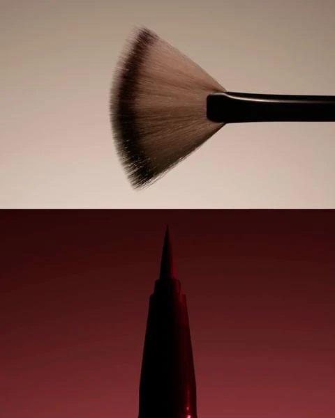 Close-up shot makeup brushes; a large fan brush with brown-tipped bristles and a black handle, and a black pointed makeup brush.