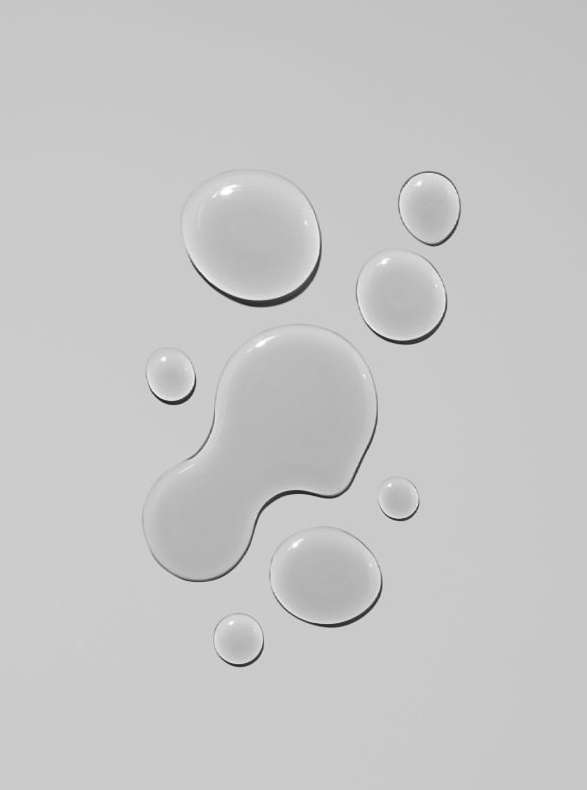 Overhead shot of clear liquid droplets on a white surface, creating a clean and minimalist abstract composition for beauty or science themes.