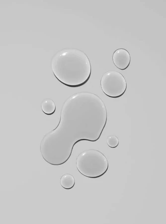 Overhead shot of clear liquid droplets on a white surface, creating a clean and minimalist abstract composition for beauty or science themes.