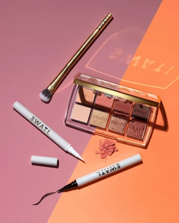 Cosmetic products including an eyeshadow palette, eyeliner pen, and makeup brush are displayed on a split pink and orange background.