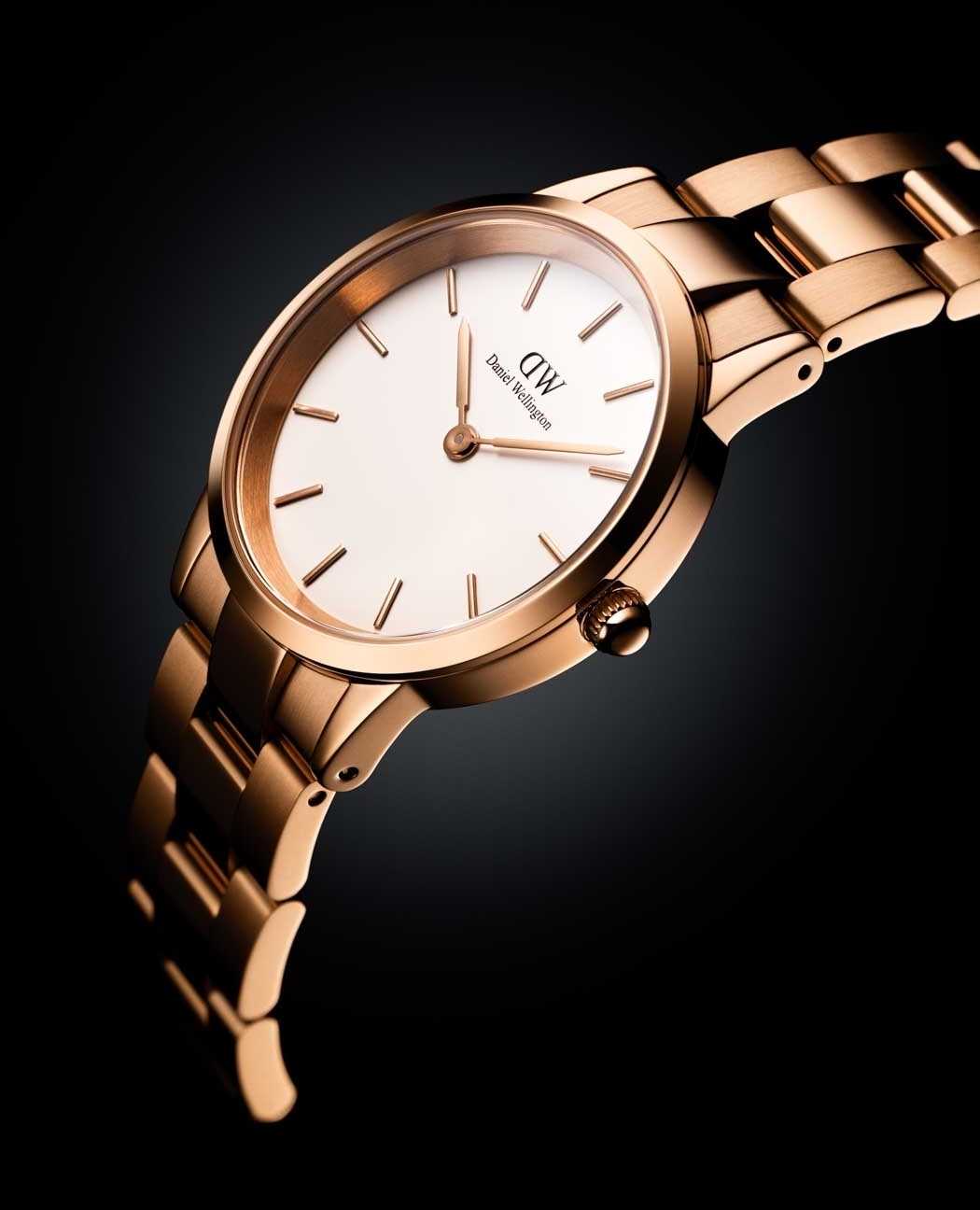 Close-up of a rose gold Daniel Wellington watch featuring a white face and a metallic band on a dark gradient background.