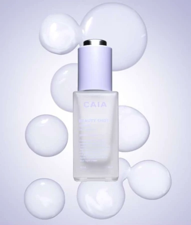 Cosmetic serum bottle with dropper top on a purple gradient background surrounded by white opaque spheres in a studio setting.