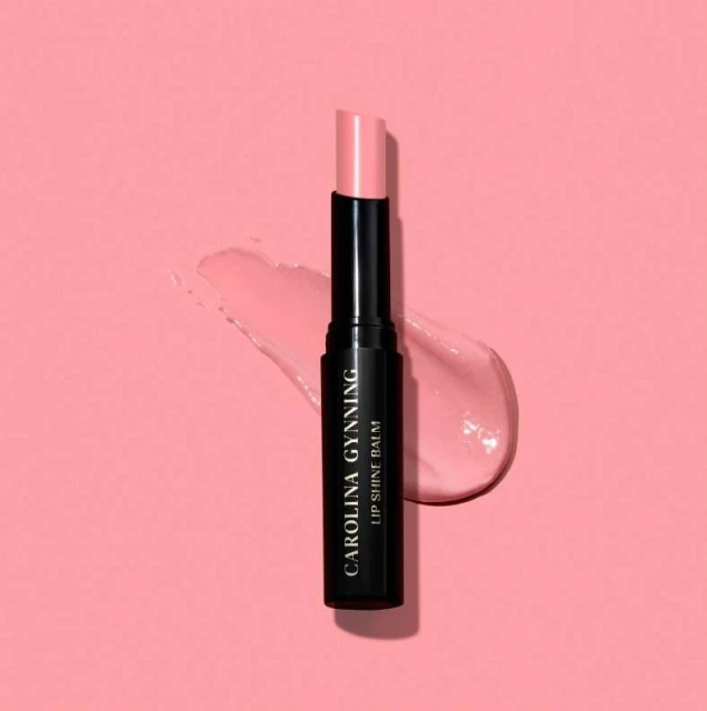 Carolina Gynning lip shine balm on a pink backdrop with a swipe of lip balm, product photography for beauty and fashion industries.