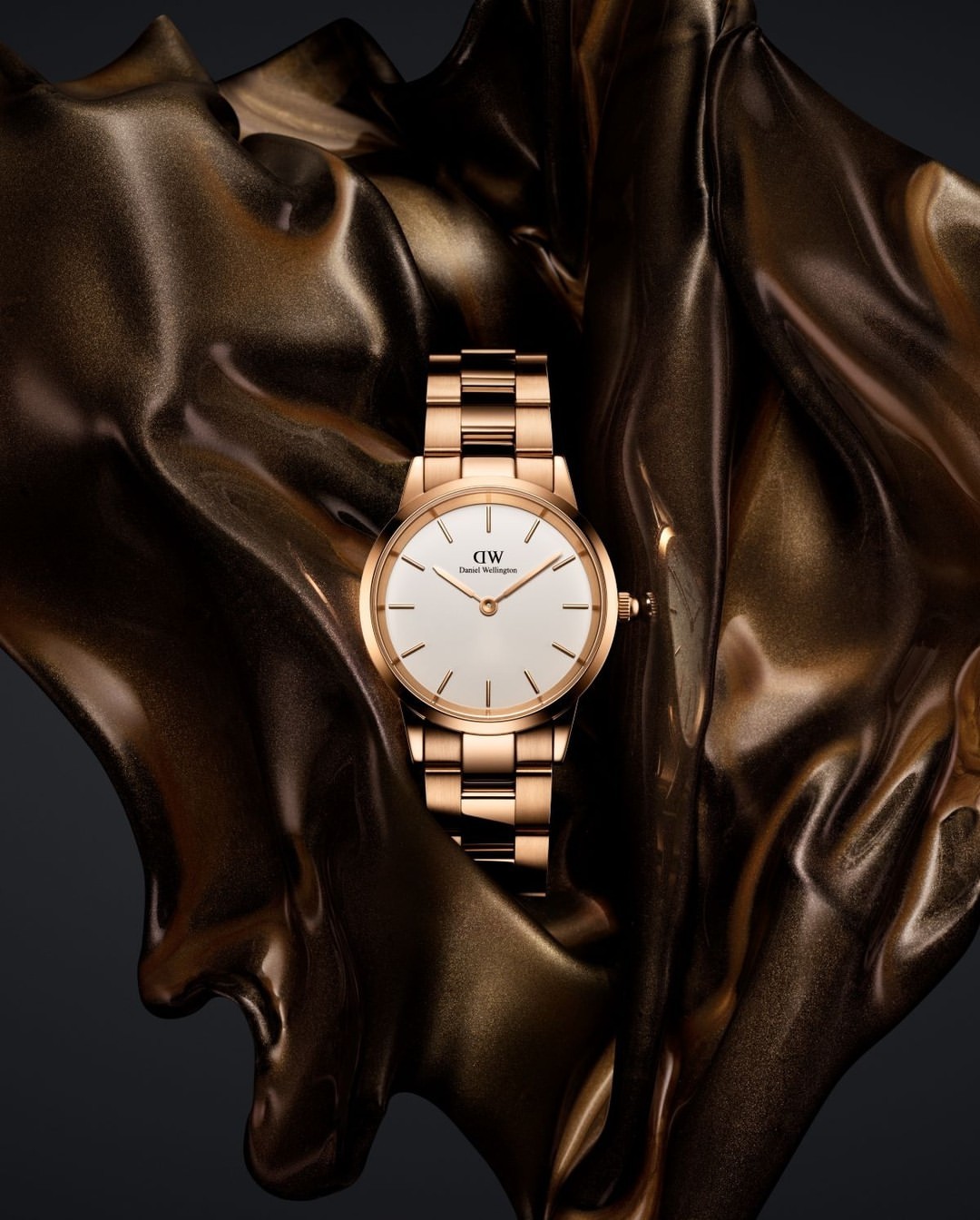 Rose gold wristwatch on a matching metallic draped background. Close-up shot highlighting the watch's design and luxury aesthetic.