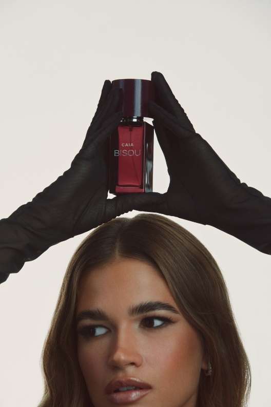 Close-up portrait of a woman holding a perfume bottle above her head wearing black gloves against a light background