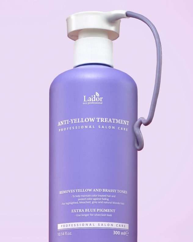 Close-up of a purple bottle of Lador anti-yellow treatment, a professional salon hair care product, on a light purple backdrop.