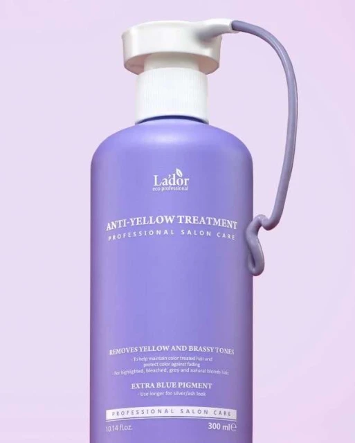 Close-up of a purple bottle of Lador anti-yellow treatment, a professional salon hair care product, on a light purple backdrop.