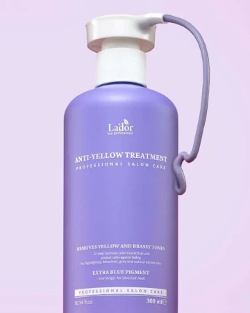 Close-up of a purple bottle of Lador anti-yellow treatment, a professional salon hair care product, on a light purple backdrop.