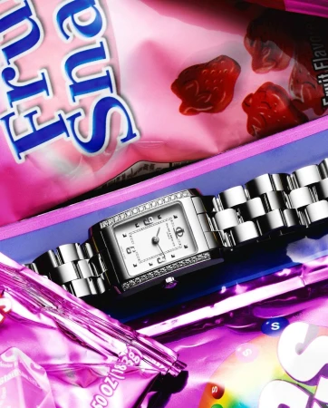 Close-up of a bejeweled silver wristwatch on candy wrappers, featuring vibrant pink, purple, red, blue, and yellow colors.