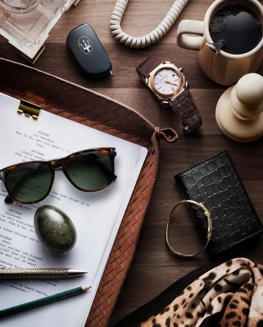 Overhead shot on a wooden surface featuring a script, sunglasses, watch, car key, coffee, wallet, bracelet, pens, and a scarf.