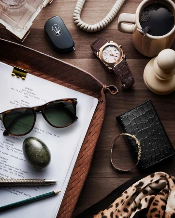 Overhead shot on a wooden surface featuring a script, sunglasses, watch, car key, coffee, wallet, bracelet, pens, and a scarf.