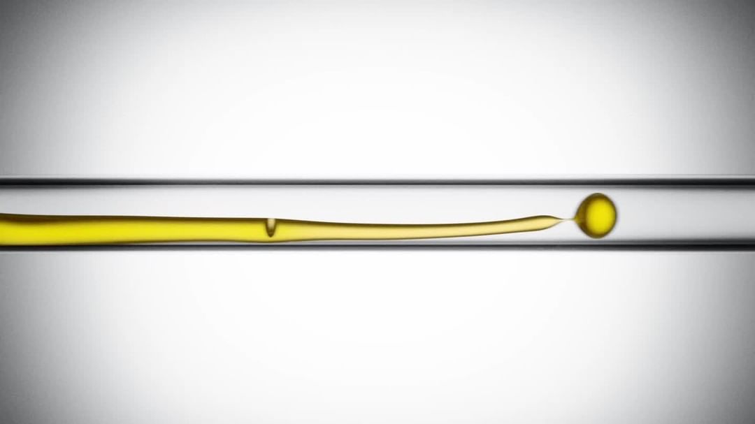 Close-up of a long, thin horizontal glass tube filled with a yellow liquid, featuring a round bubble at the right end.