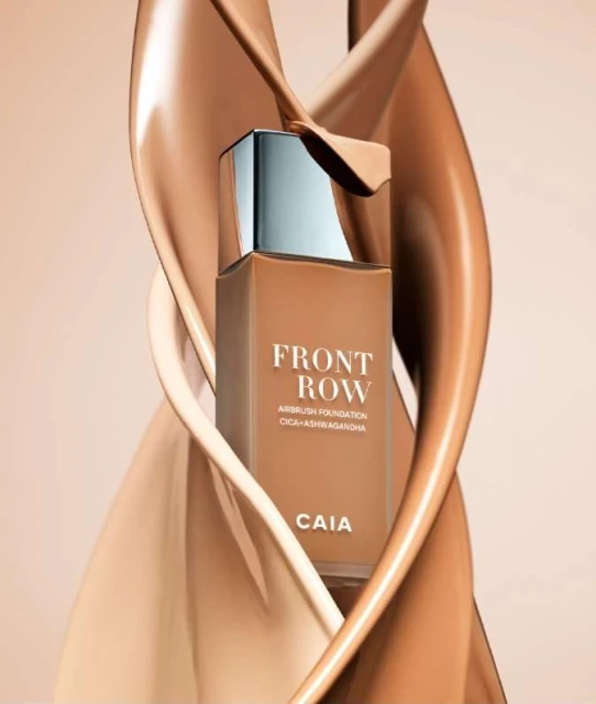 CAIA Cosmetics Front Row foundation product shot with light brown and beige creamy textures in the background on a neutral backdrop.