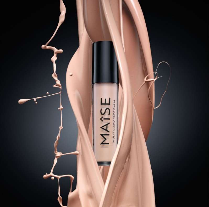 Maise Multi Glow Face Balm product shot surrounded by splashes of nude makeup in a studio setting against a dark background.