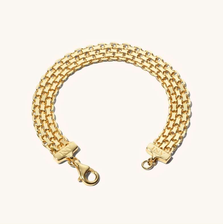 Close-up of a gold-toned metal bracelet composed of interconnected links, resting on a soft, off-white background.