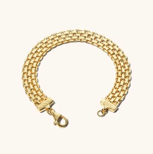 Close-up of a gold-toned metal bracelet composed of interconnected links, resting on a soft, off-white background.