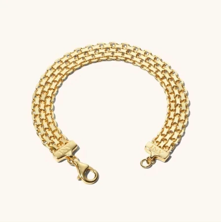 Close-up of a gold-toned metal bracelet composed of interconnected links, resting on a soft, off-white background.