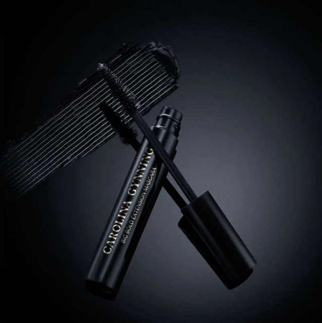 Close-up of Carolina Gynning Big Bold Extension Mascara tube and applicator wand with black mascara streak on a dark background.