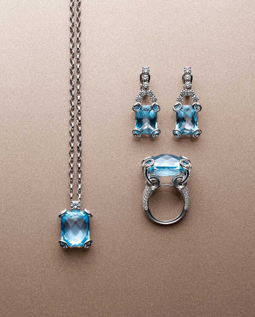 Elegant jewelry set featuring a necklace, a ring and matching earrings with rectangular light blue gemstones and silver settings.
