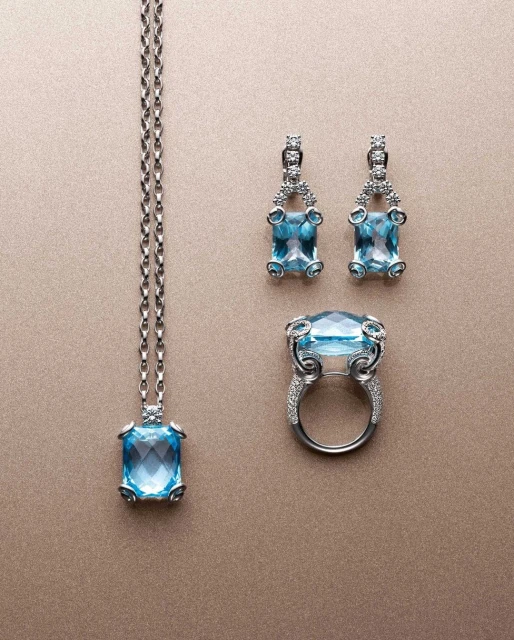 Elegant jewelry set featuring a necklace, a ring and matching earrings with rectangular light blue gemstones and silver settings.