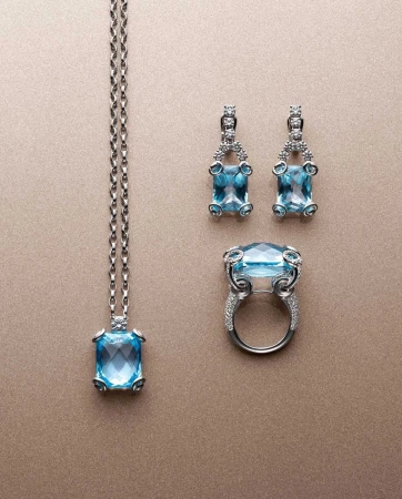 Elegant jewelry set featuring a necklace, a ring and matching earrings with rectangular light blue gemstones and silver settings.