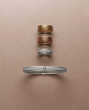 Still life featuring a silver bracelet and gold, rose gold, and silver rings with a woven design arranged on a tan background.