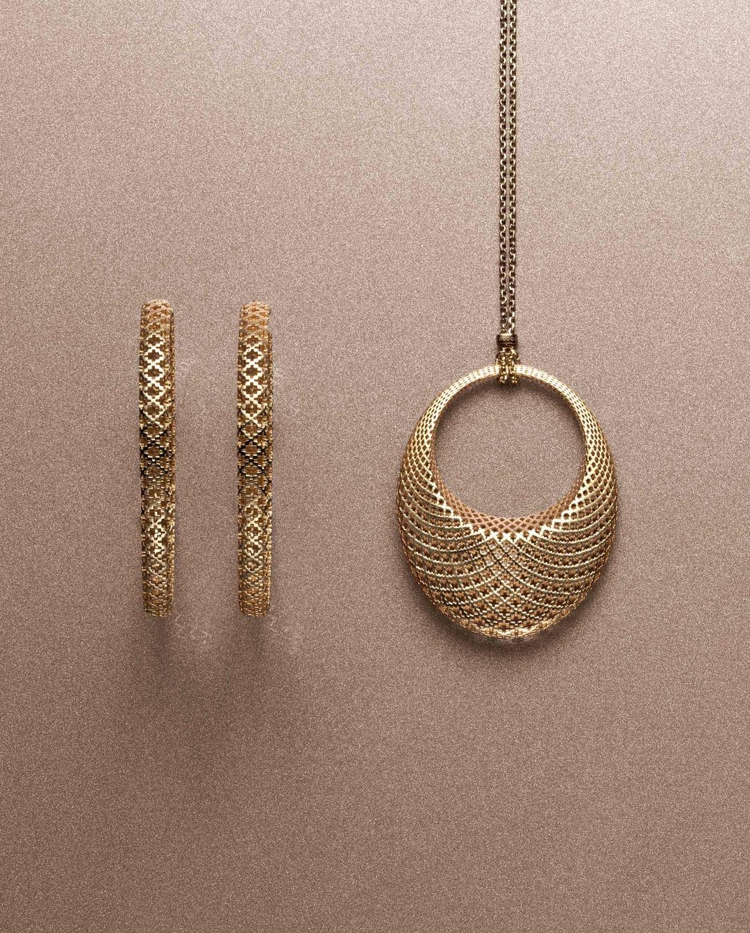 Elegant gold jewelry set featuring hoop earrings and a pendant necklace with intricate lattice design against a neutral backdrop.