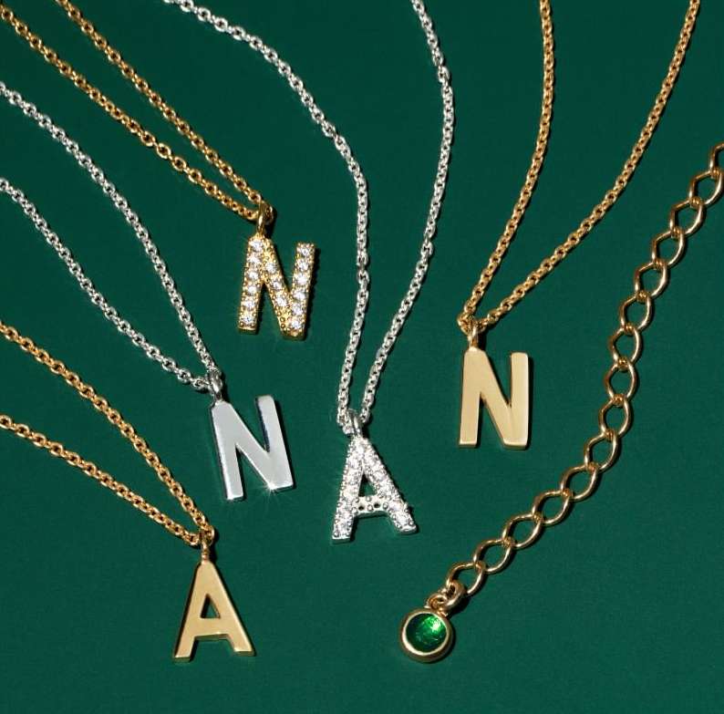 A close-up showcases gold and silver necklaces with initial pendants, set against a dark green background. Each letter is styled differently.