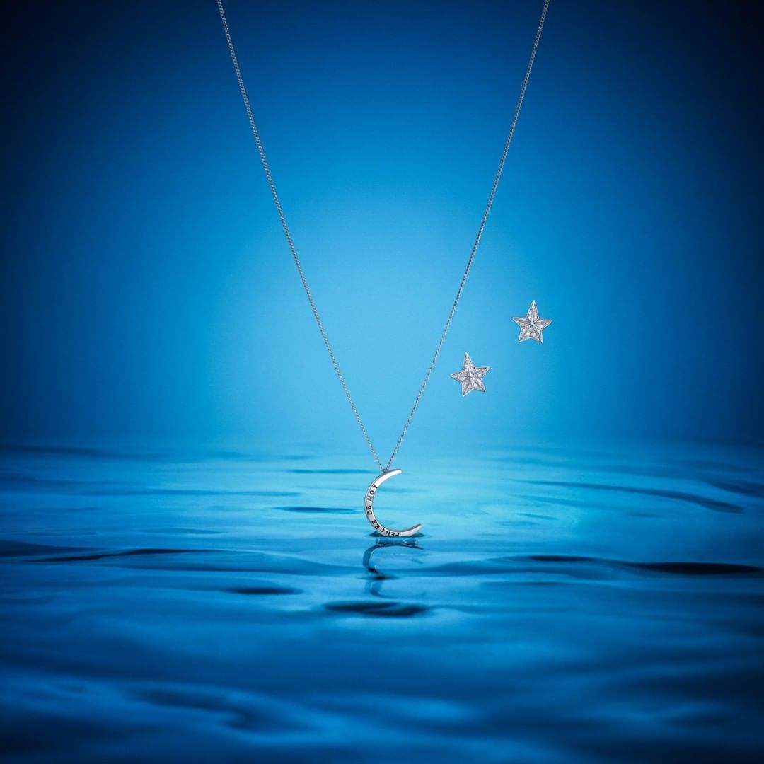 Elegant jewelry set on a shimmering blue surface: a crescent moon pendant necklace and matching star-shaped stud earrings.
