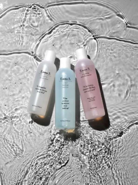 Three colorful Emma S. cleansing water bottles arranged in a line and photographed under rippling water creating abstract patterns.