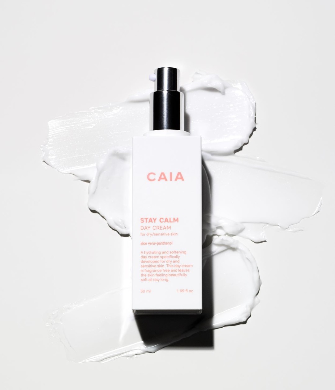 Product shot of a CAIA Cosmetics Stay Calm Day Cream bottle on a white surface with a smear of white cream.