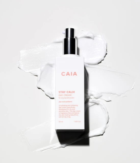 Product shot of a CAIA Cosmetics Stay Calm Day Cream bottle on a white surface with a smear of white cream.