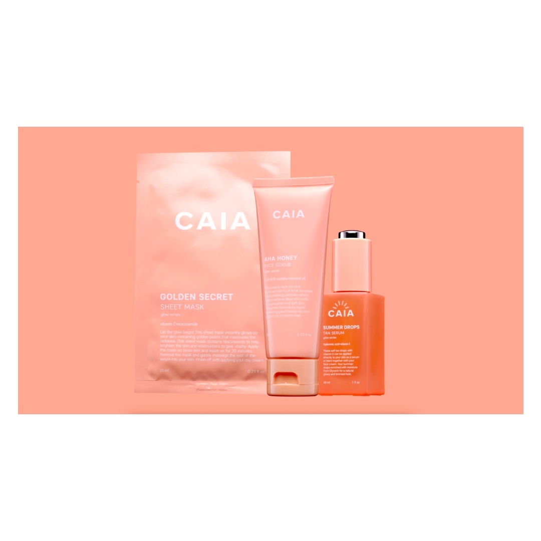 Three pink and orange CAIA cosmetic products: a sheet mask, moisturizer tube, and serum, all displayed against a matching pink background.