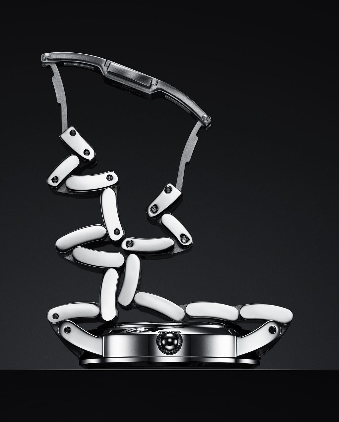 Elevated product shot of a silver and white watch with a deconstructed, sculptural metal band on a dark reflective surface.