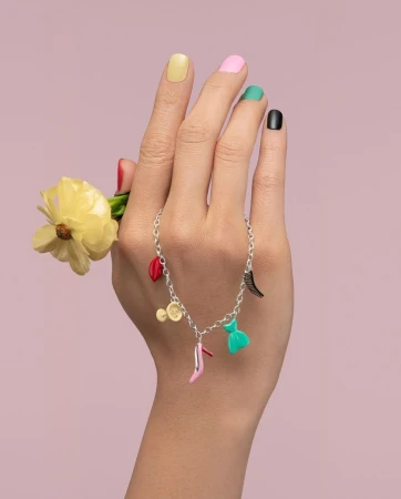 Close-up of a hand holding a yellow flower and adorned with a charm bracelet featuring colorful charms against a light purple backdrop.