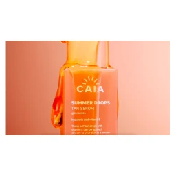 Caia Summer Drops tan serum bottle with amber liquid dripping down the side against a warm peach studio background