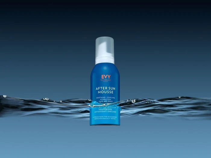 Blue bottle of EVY After Sun Mousse emerging from dark water with ripples against a blue gradient background