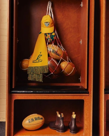 Locker room display with rugby balls, Wallabies scarf, cap, and boots arranged in wood locker with overhead and shelf storage.