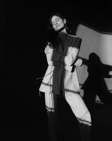 Monochrome portrait of a woman in a tailored suit posing with eyes closed against a light wall with dramatic striped shadows