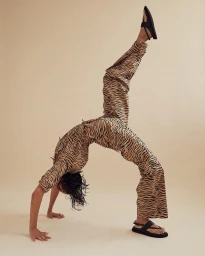 Model in tiger-print matching set doing a backbend in black sandals against a solid beige seamless background