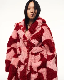 Model wearing a pink and red patterned shearling coat against a plain white background by Daniel Nadel.