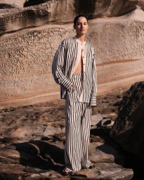 Model standing on rocky terrain wearing a matching striped button-down shirt and trousers with dark sandals.