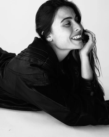 Monochrome portrait of a smiling young woman wearing a black leather jacket against a seamless white background.