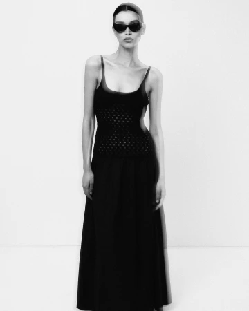 Model in black sunglasses and a dark sleeveless maxi dress against a plain white studio background.