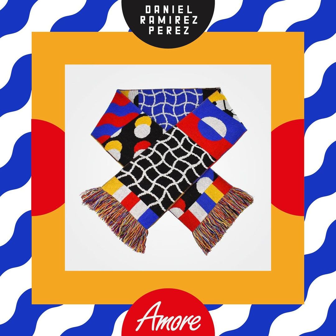 Colorful knitted scarf with geometric patterns of circles, squares, and lines in red, yellow, blue, and black. Square white background.
