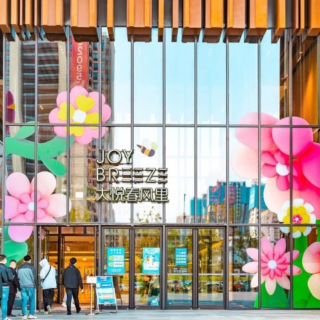 Exterior of Joy Breeze shopping center with floral decorations and people entering, featuring a modern urban design with glass and wood.