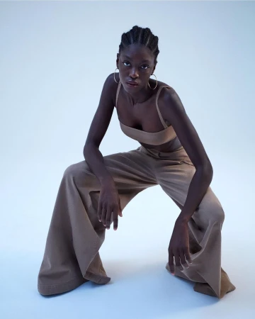 Black woman in beige crop top and wide-leg trousers crouching against a seamless white studio background