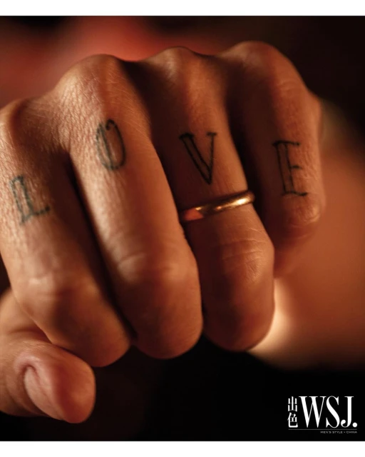Close-up of a human fist with the word 'LOVE' tattooed on the fingers, featuring a gold ring on the ring finger and WSJ logo.