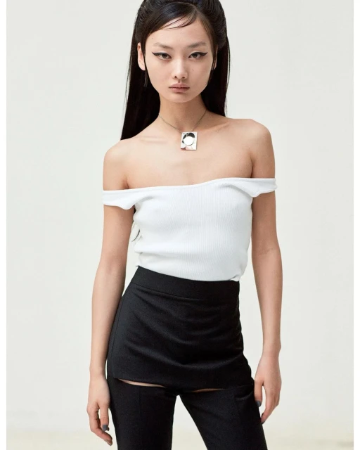 Studio shot of an adult woman wearing a white, off-the-shoulder top, black bottoms, and a silver necklace against a neutral background.